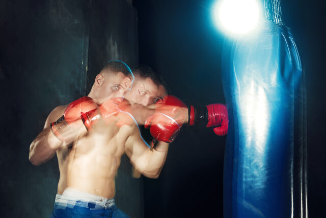 Male boxer boxing in punching bag with dramatic edgy lighting in a dark studio